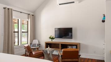 A hotel room with a bed, a desk with a chair, a television, and an air conditioning unit.