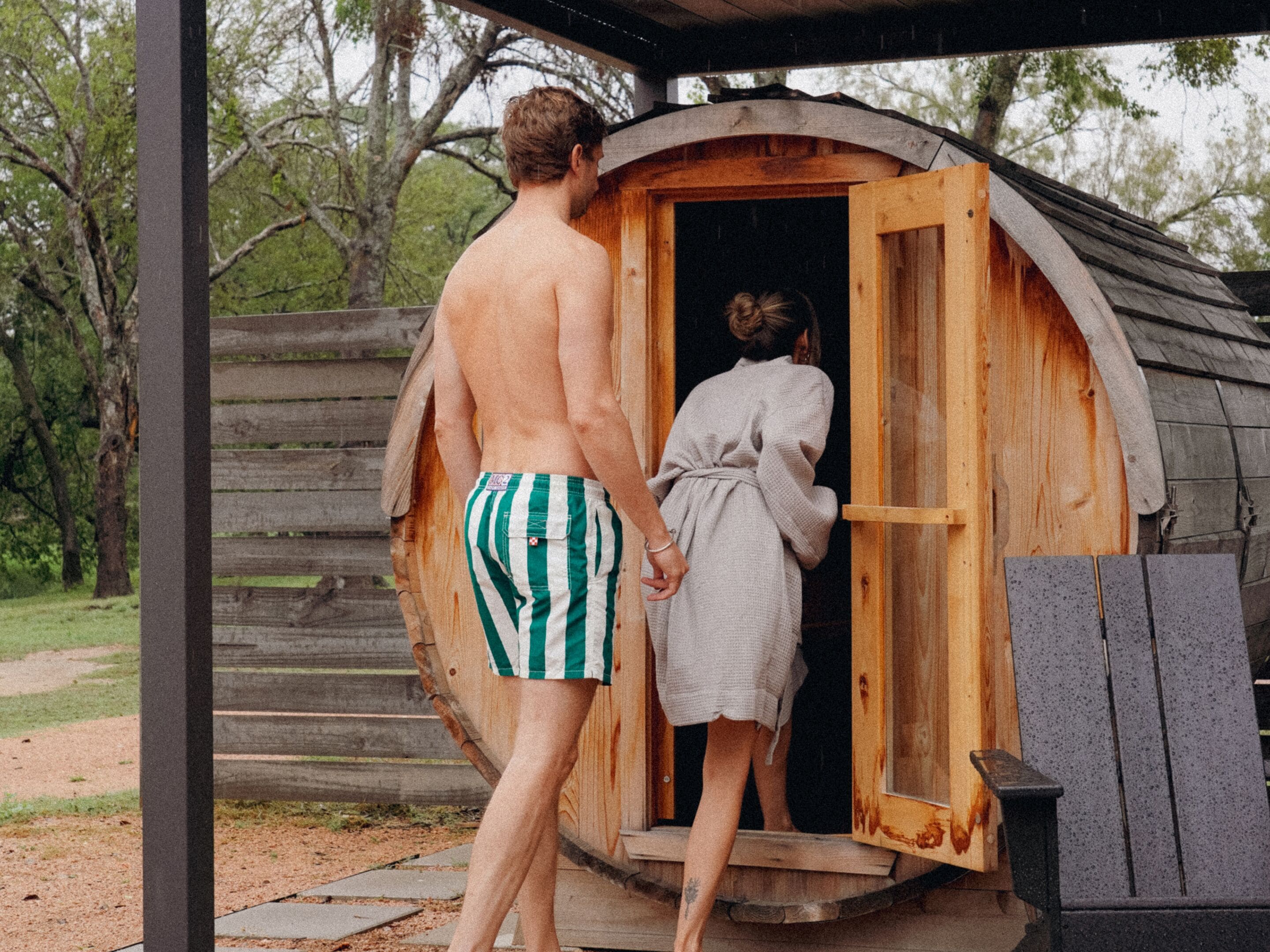 A wooden cabin with a single door, a wooden deck, and a metal bench.
