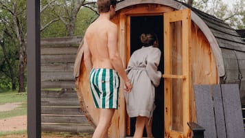A wooden cabin with a single door, a wooden deck, and a metal bench.
