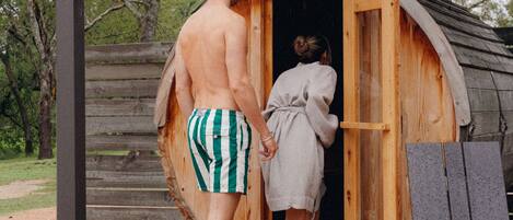 A wooden cabin with a single door, a wooden deck, and a metal bench.