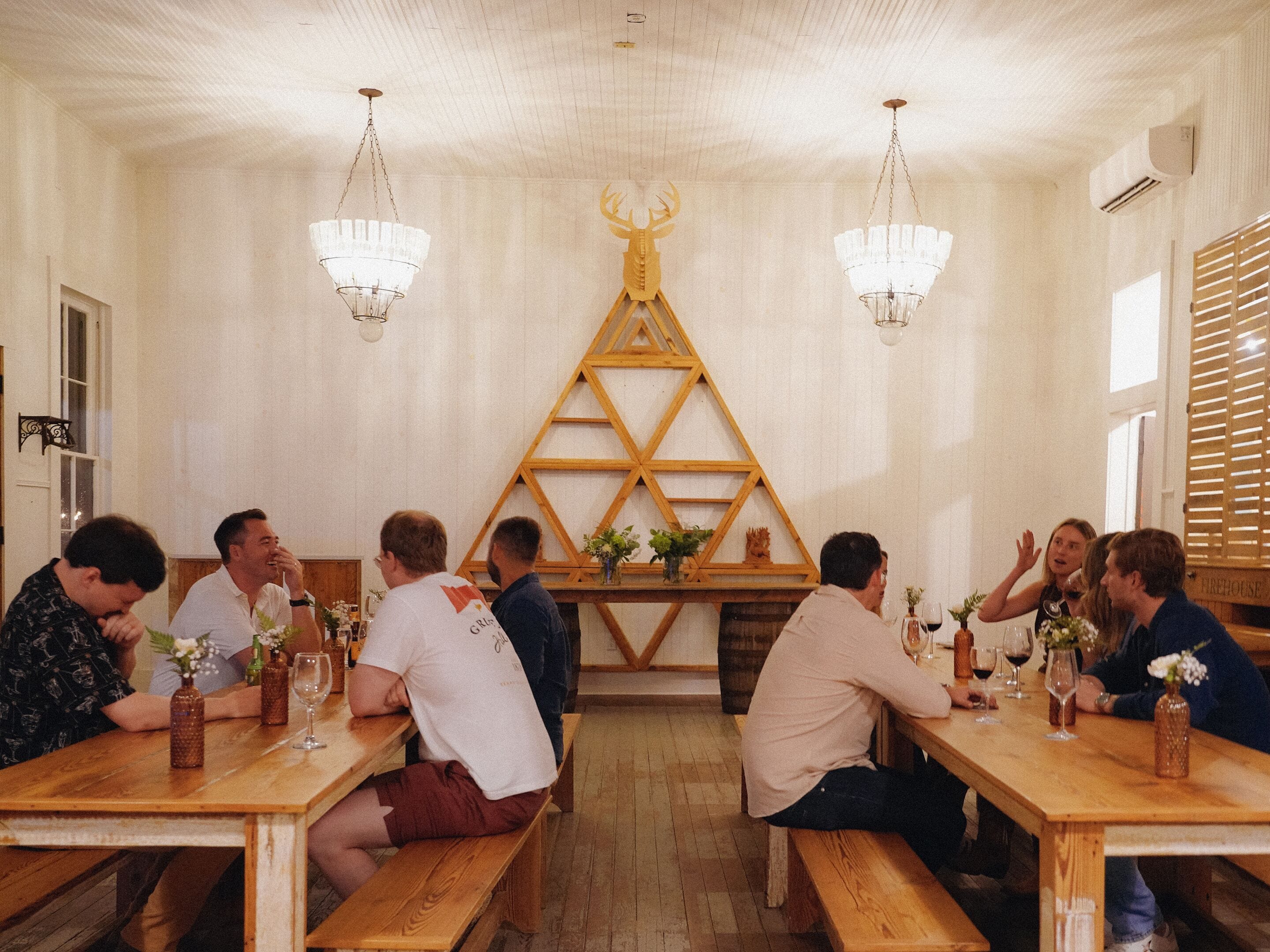 Un espace repas avec des bancs et des tables en bois, une décoration murale en bois et des lustres suspendus.