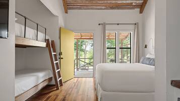A bedroom with a bunk bed, a single bed, wooden flooring, a yellow door, and a view of the outdoors.