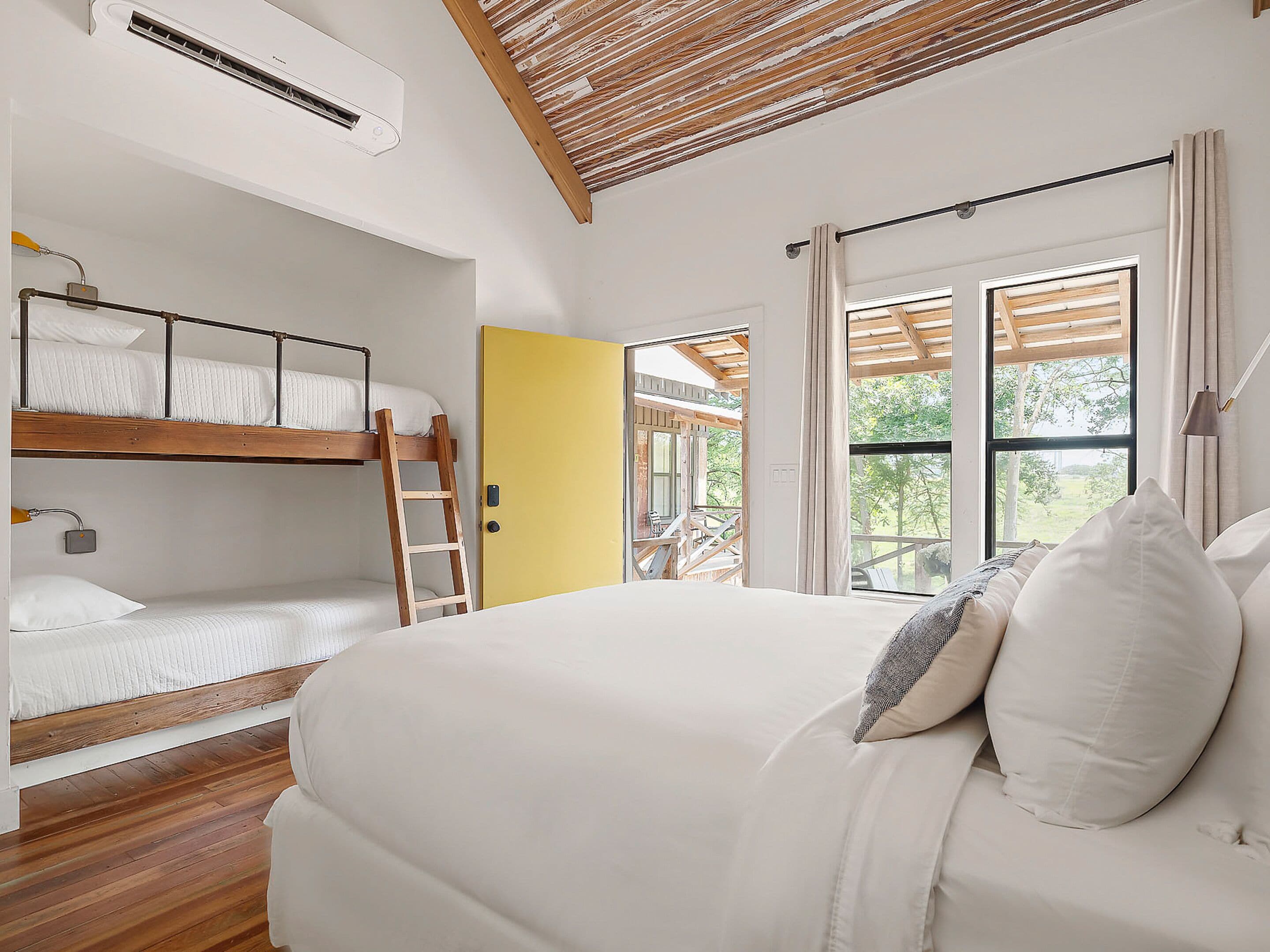 Una camera da letto con un letto a castello, un letto singolo, pavimento in legno, ventilatore a soffitto e vista all'esterno.
