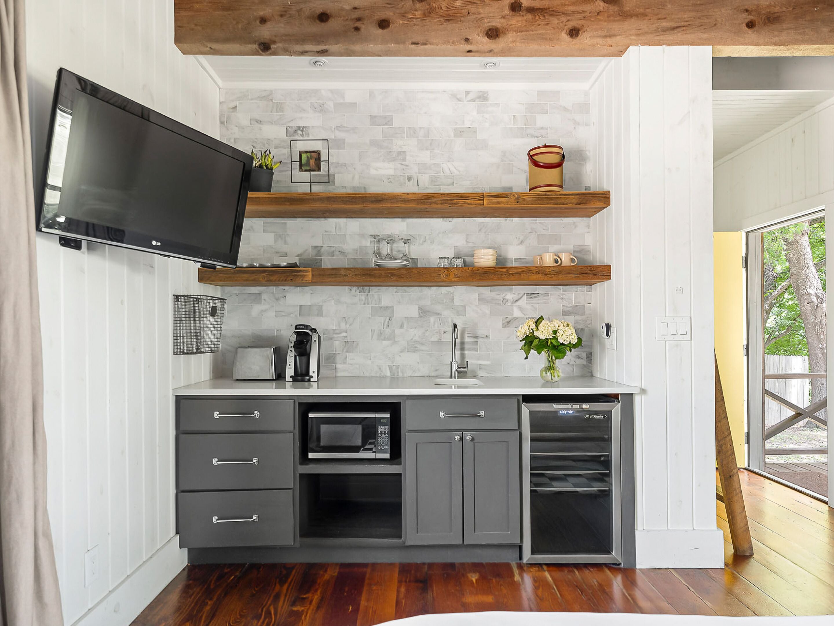 A modern kitchen with a flat-screen TV, wooden shelves, a microwave, and a dishwasher.
