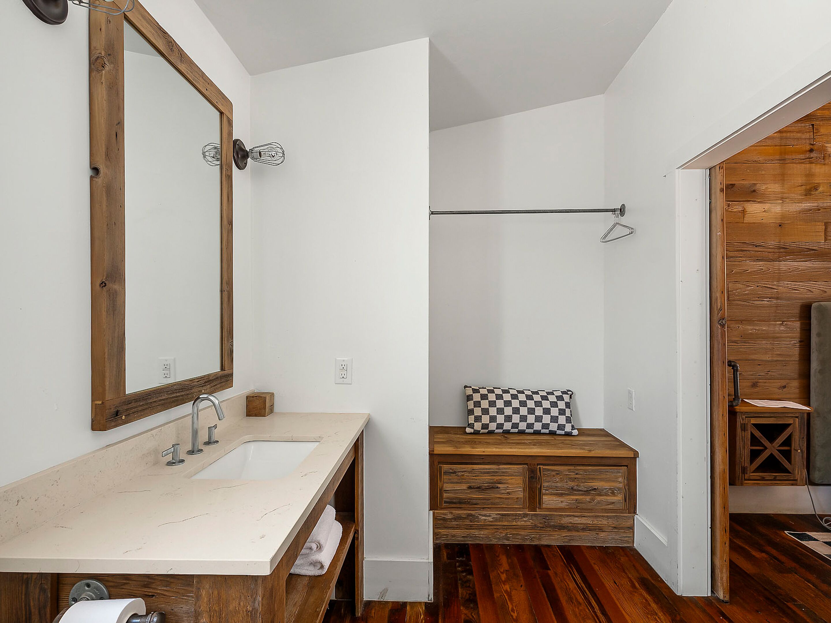 Une salle de bain avec un meuble-lavabo en bois, un grand miroir, un porte-serviettes et un coussin à carreaux.