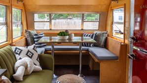 Interior acolhedor de uma caravana, com área de estar que inclui uma mesa, almofadas e vista para o exterior.