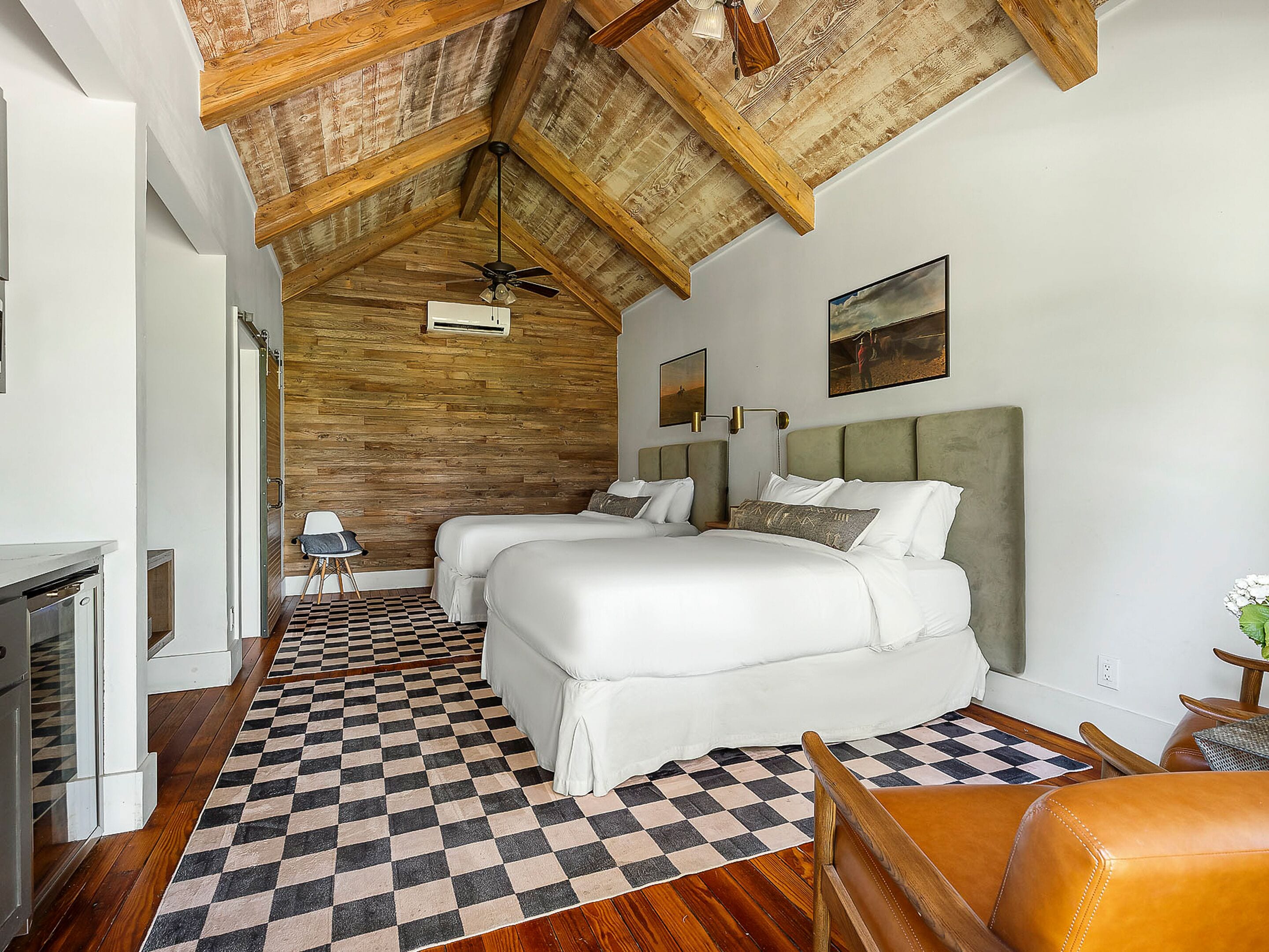 A bedroom with a checkered floor, two beds, a ceiling fan, and a painting on the wall.