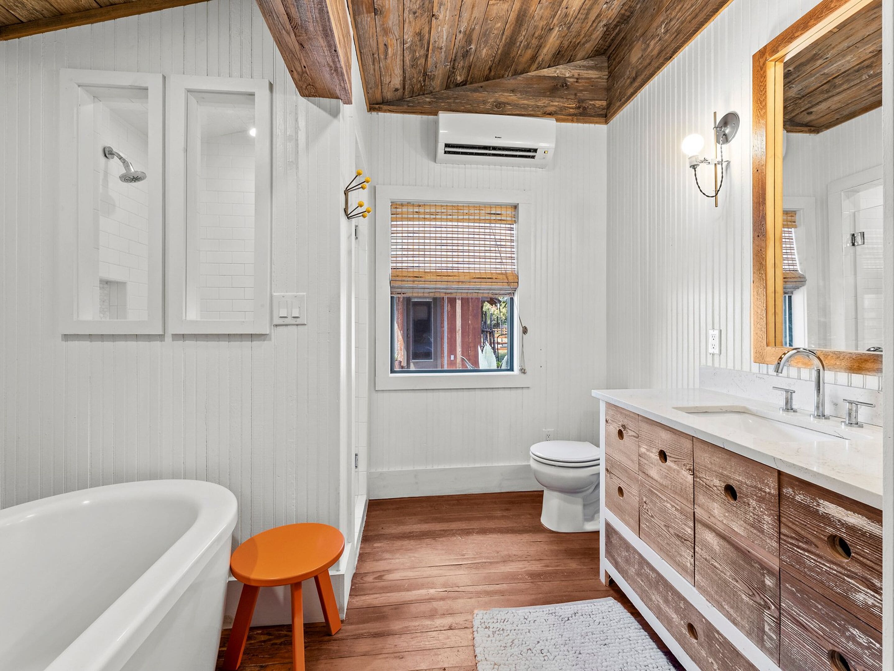 A bathroom with a wooden floor, white walls, a bathtub, a toilet, and a vanity with a mirror.
