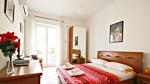 A bedroom with a wooden bed, a nightstand, a desk with a vase of flowers, and a large window. - Stairs of Trastevere (Rome)