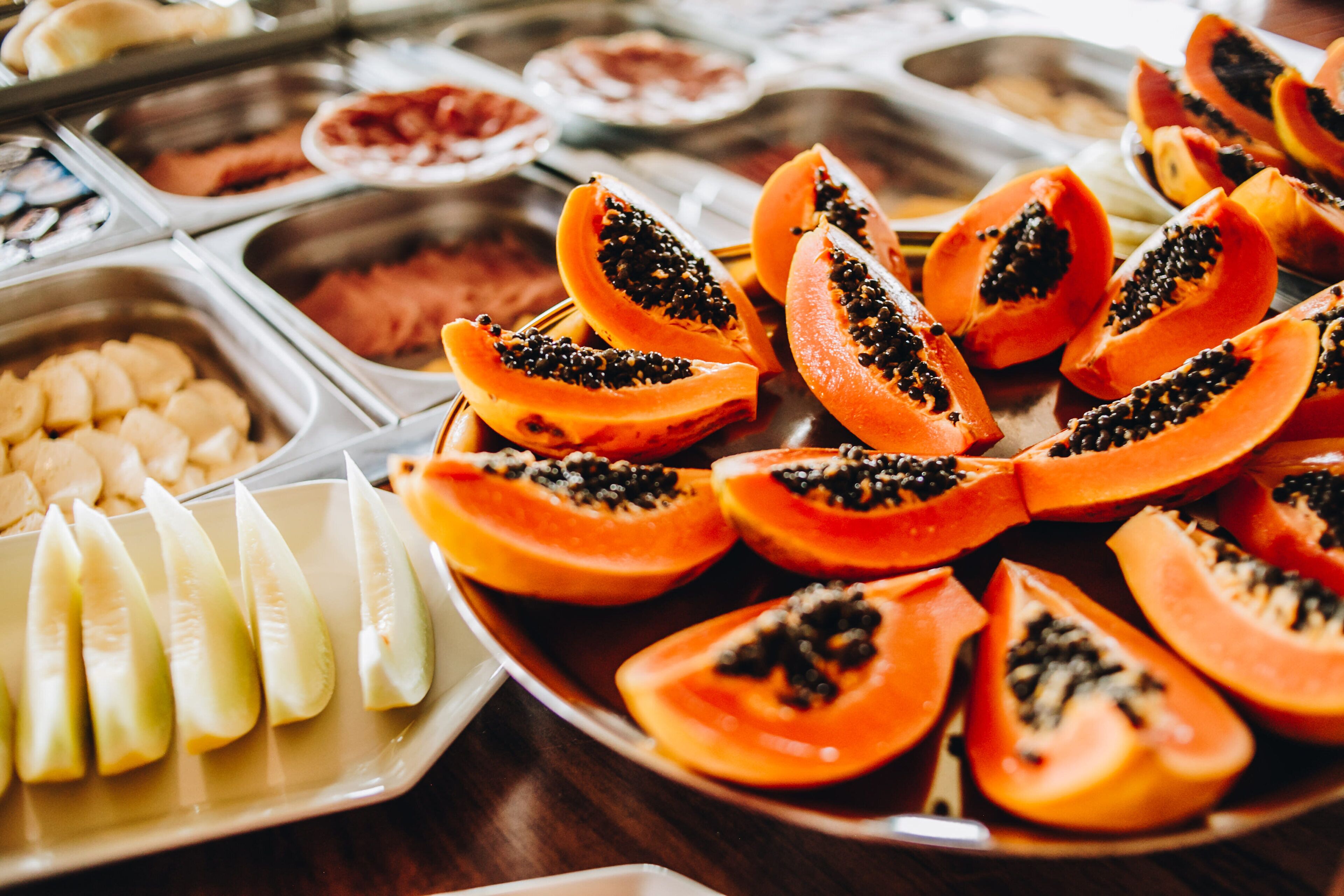 Een buffet met diverse gerechten, waaronder plakjes papaya.
