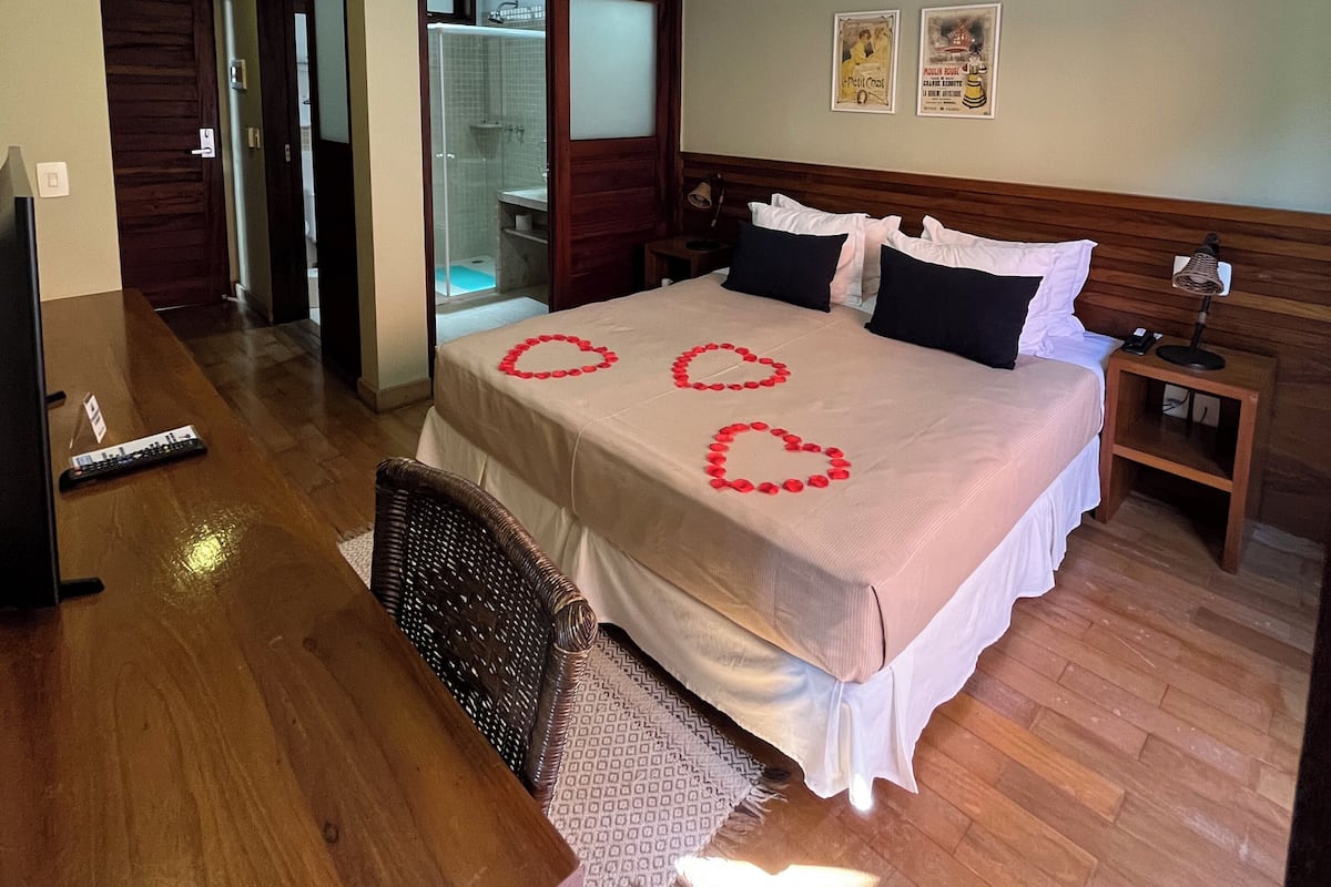 A hotel room with a bed, a desk, a chair, a nightstand, a ceiling fan, and a shower area.