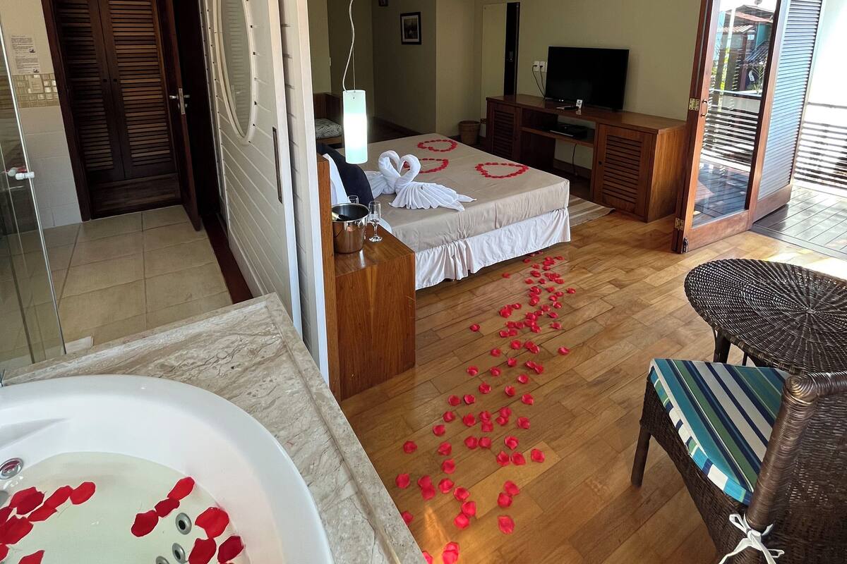 A hotel room with a bed, a TV, a desk, a chair, a balcony, and a bathroom with a bathtub.