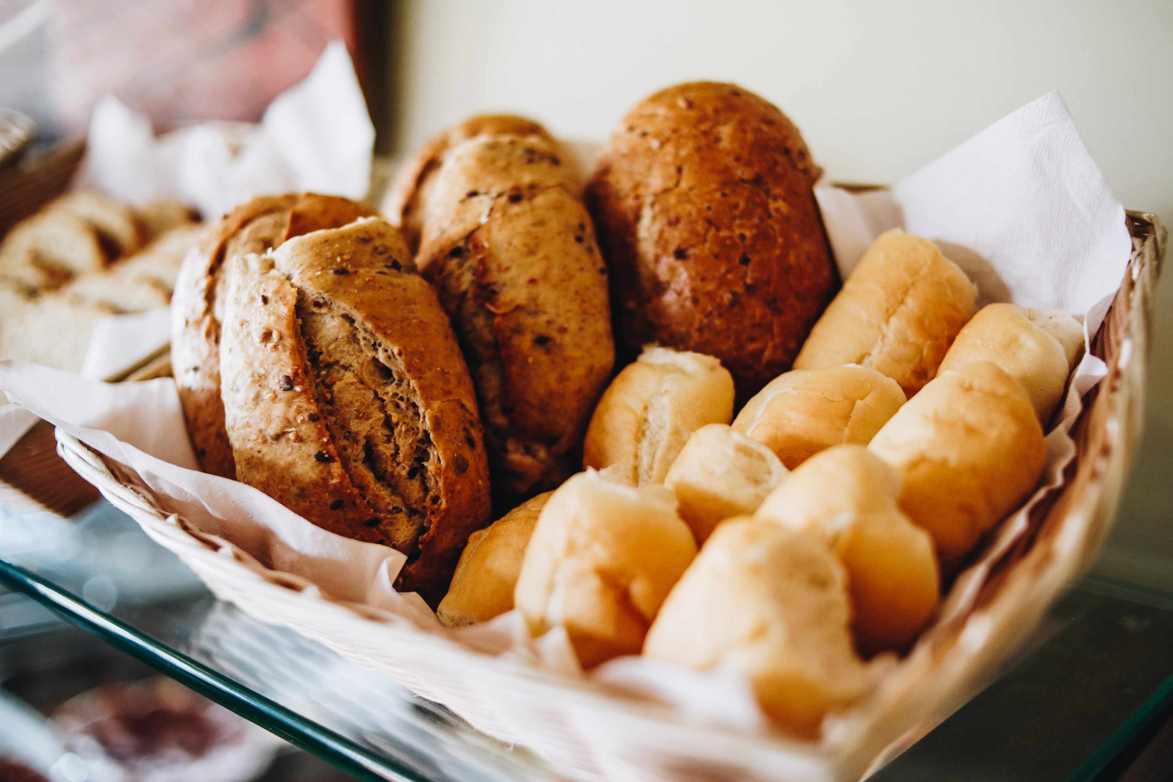 A basket of various breads, including rolls and baguettes, displayed in a bakery setting.