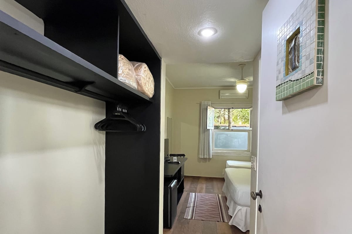 A narrow hallway with a bed, a desk, and a shelf with bags.