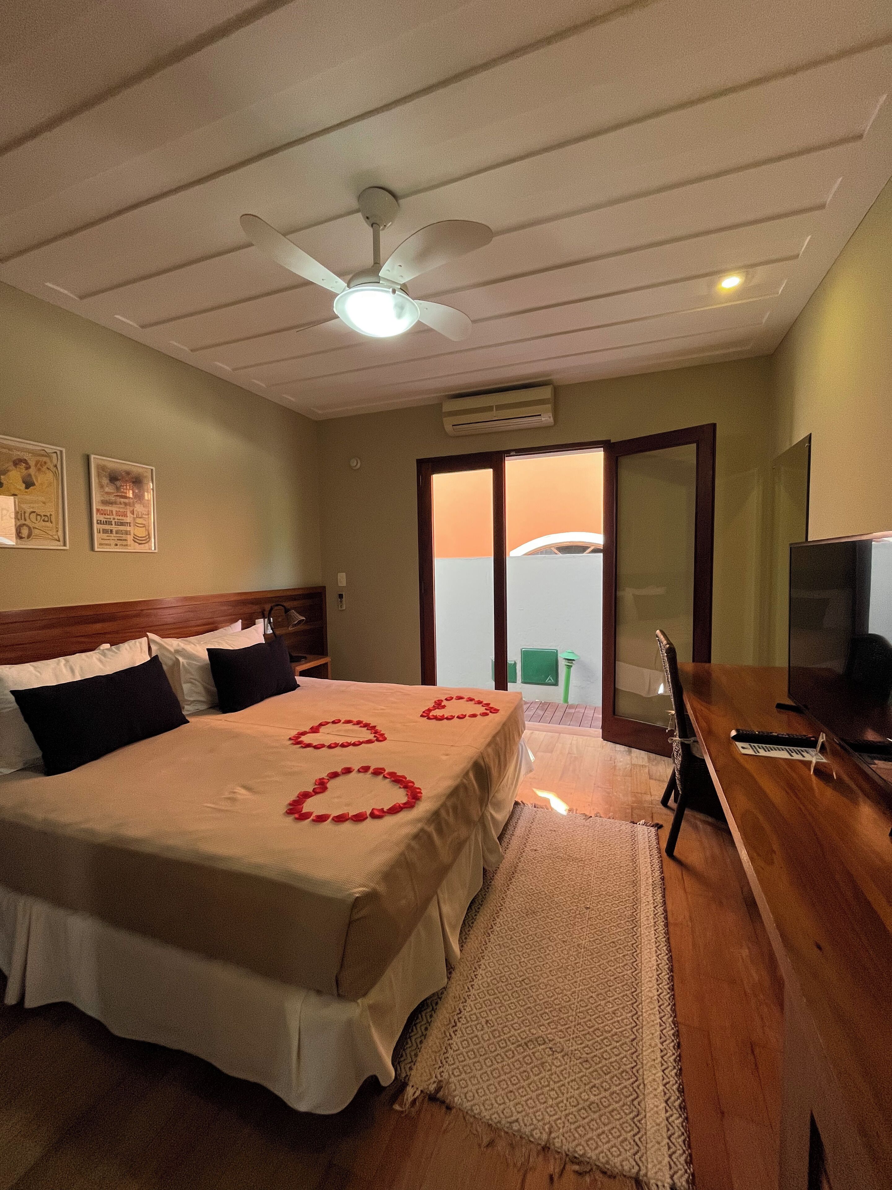 A hotel room with a bed, a desk, a chair, a television, and a ceiling fan.