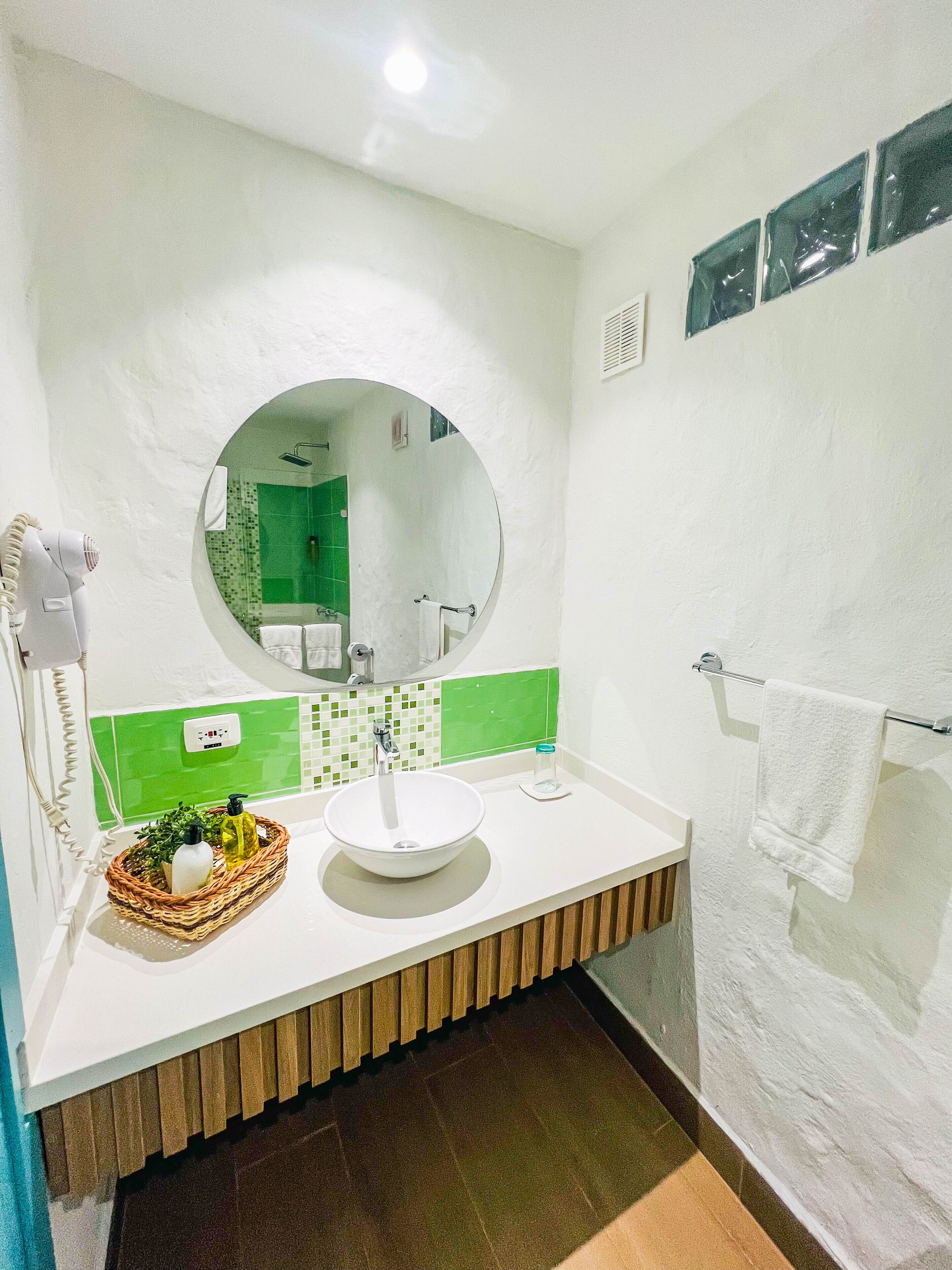 Un baño con lavamanos blanco, espejo redondo y salpicadero de azulejos verdes.