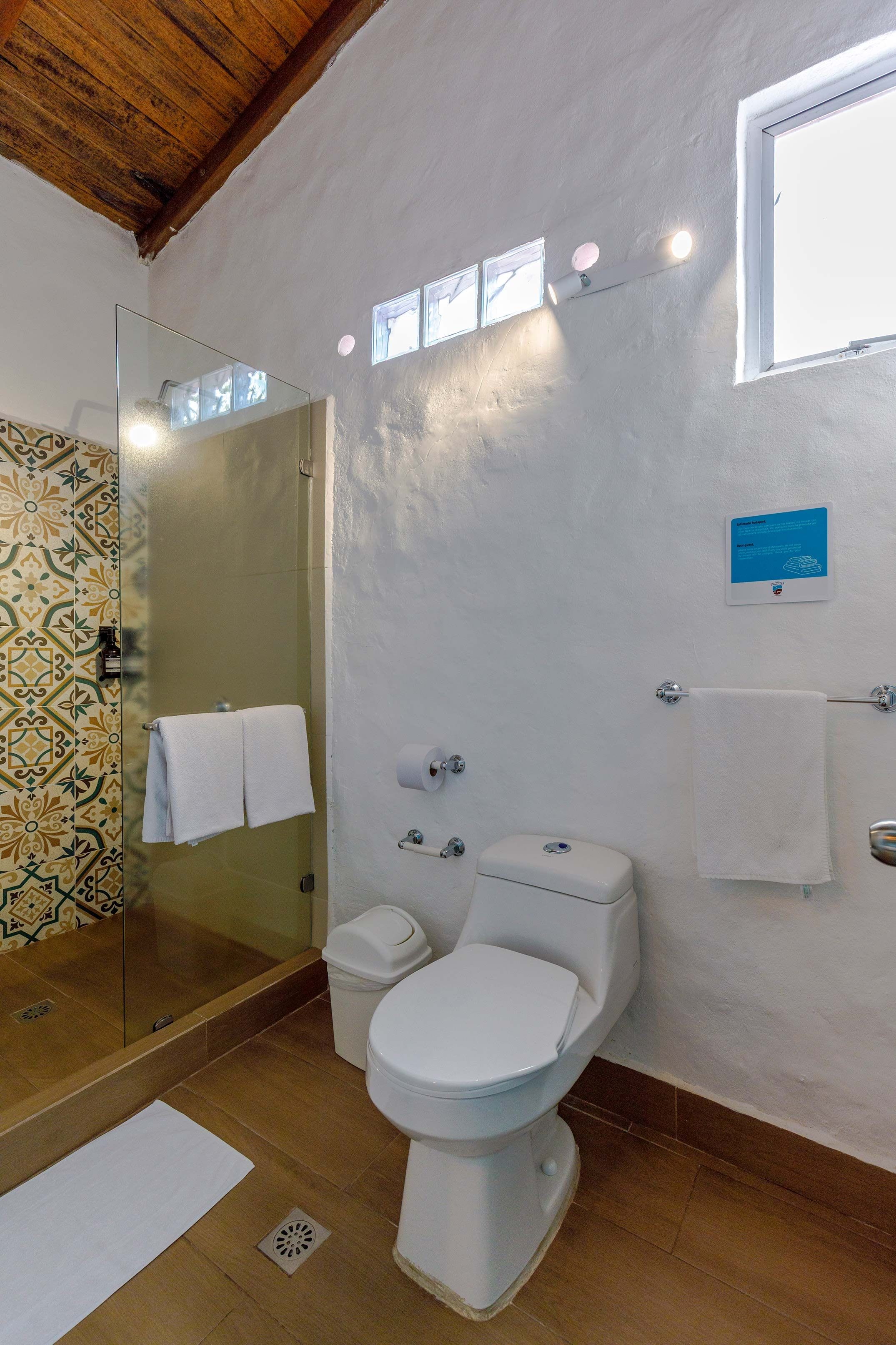 A bathroom with a toilet, a glass shower enclosure, a towel rack, and a wall-mounted light fixture.