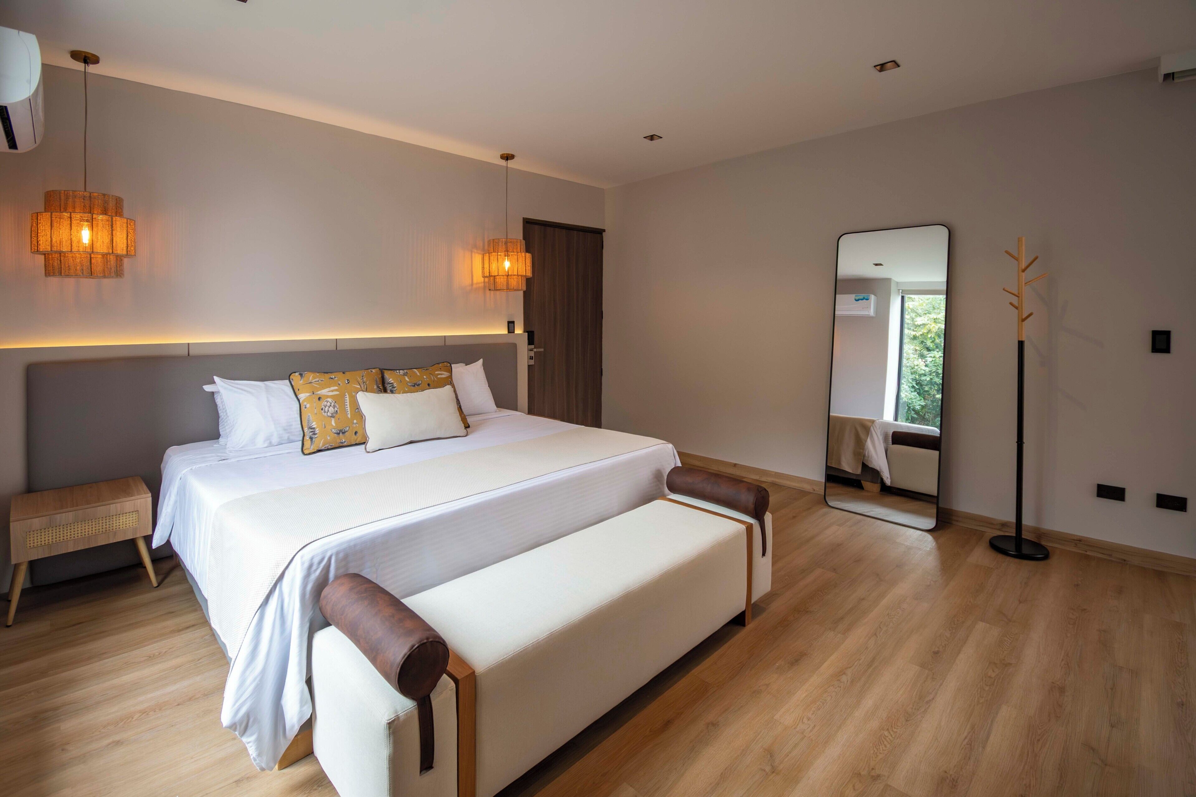 A modern bedroom with a large bed, bedside lamps, a mirror, and a wooden floor.