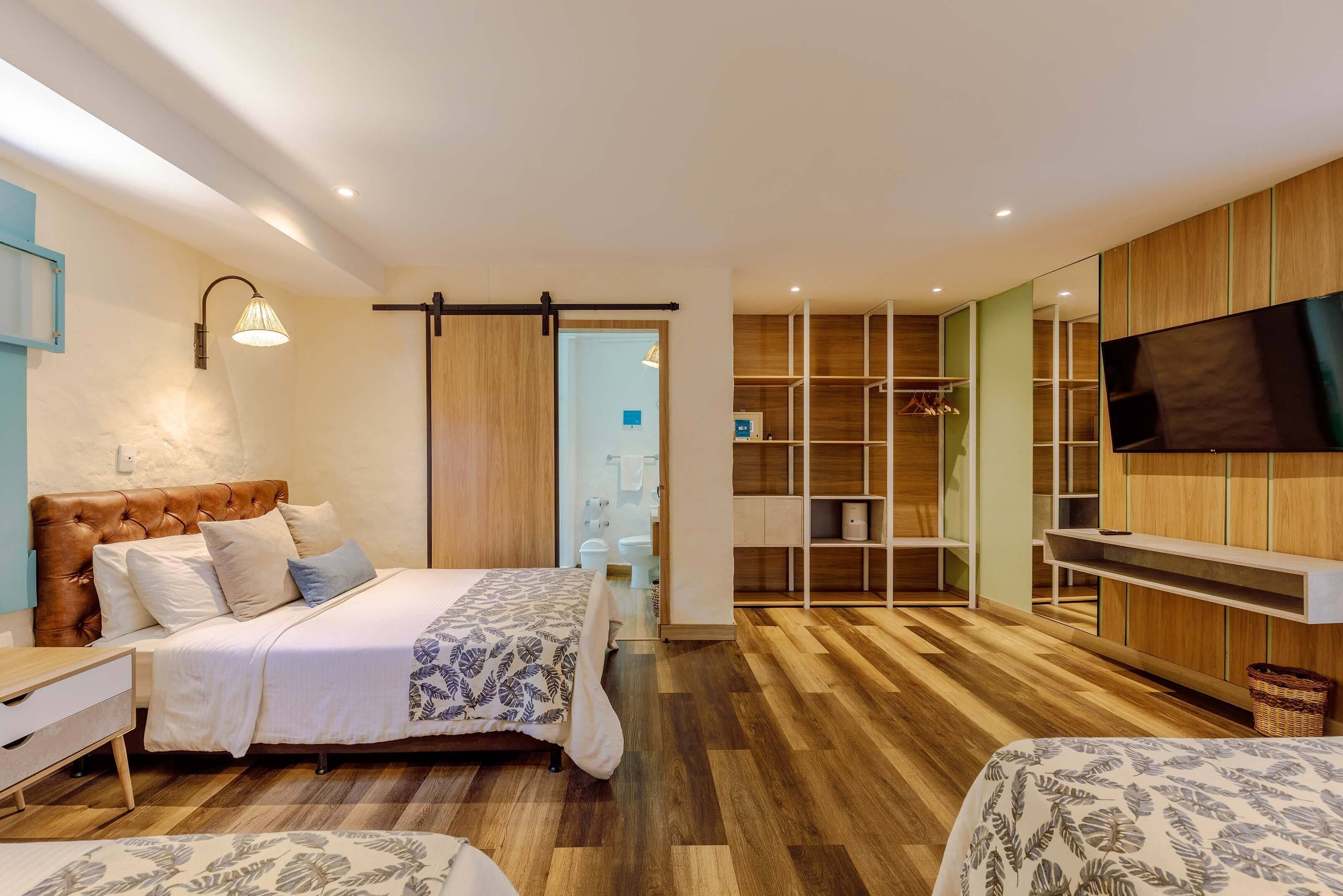 Ein modernes Schlafzimmer mit einem großen Bett, einem Kleiderschrank, einem Fernseher und einem durch eine Schiebetür einsehbarer Badezimmer.