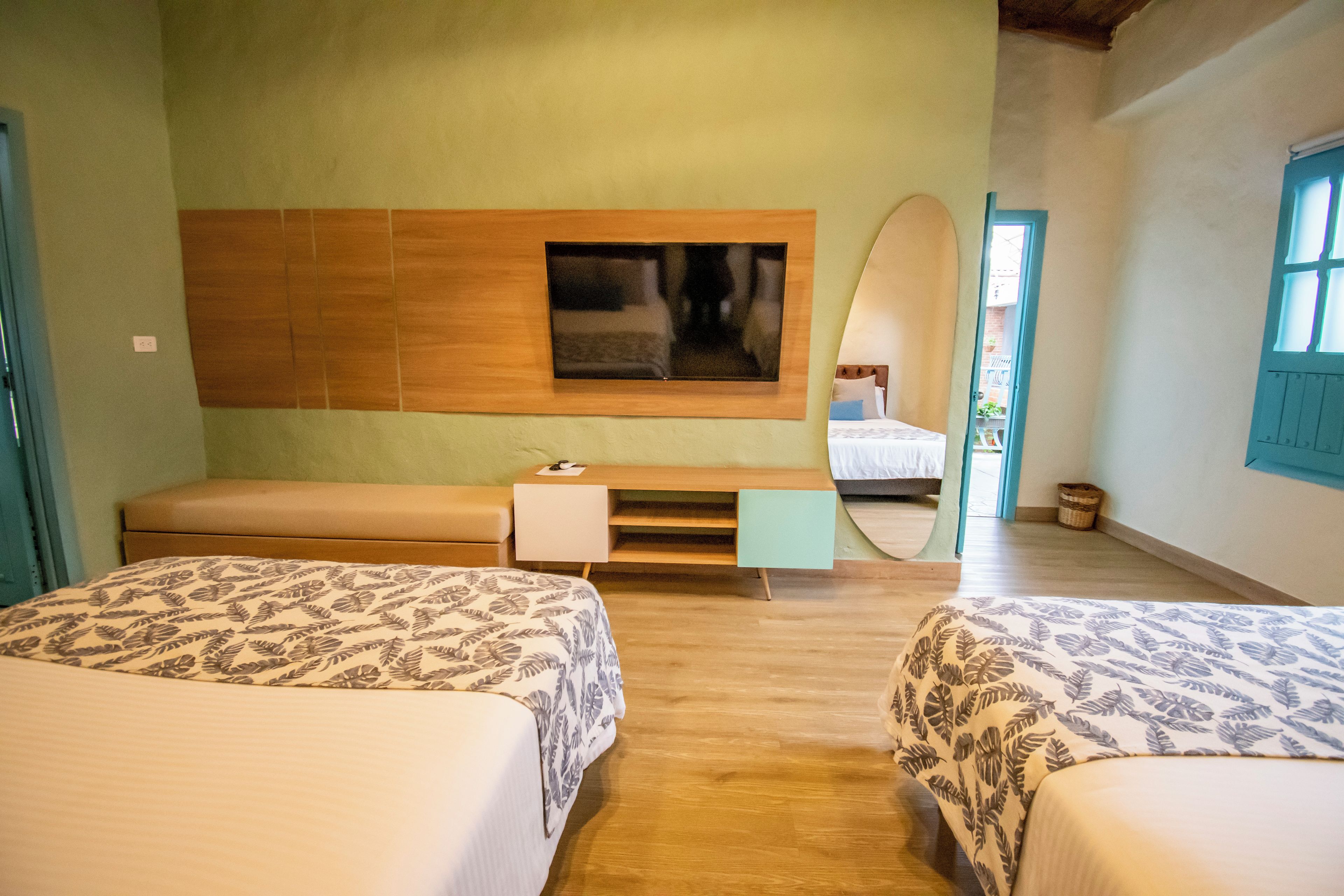 Ein Hotelzimmer mit zwei Betten, einem Holzkopfteil, einem flachbildfernseher an der Wand, einem kleinen Nachttisch und einem großen Spiegel.