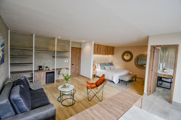 A modern hotel room with a sofa, a coffee table, a leather chair, a bed, a bedside table, a mirror, and a small kitchenette. - Hotel Salento Real Eje Cafetero (Salento)