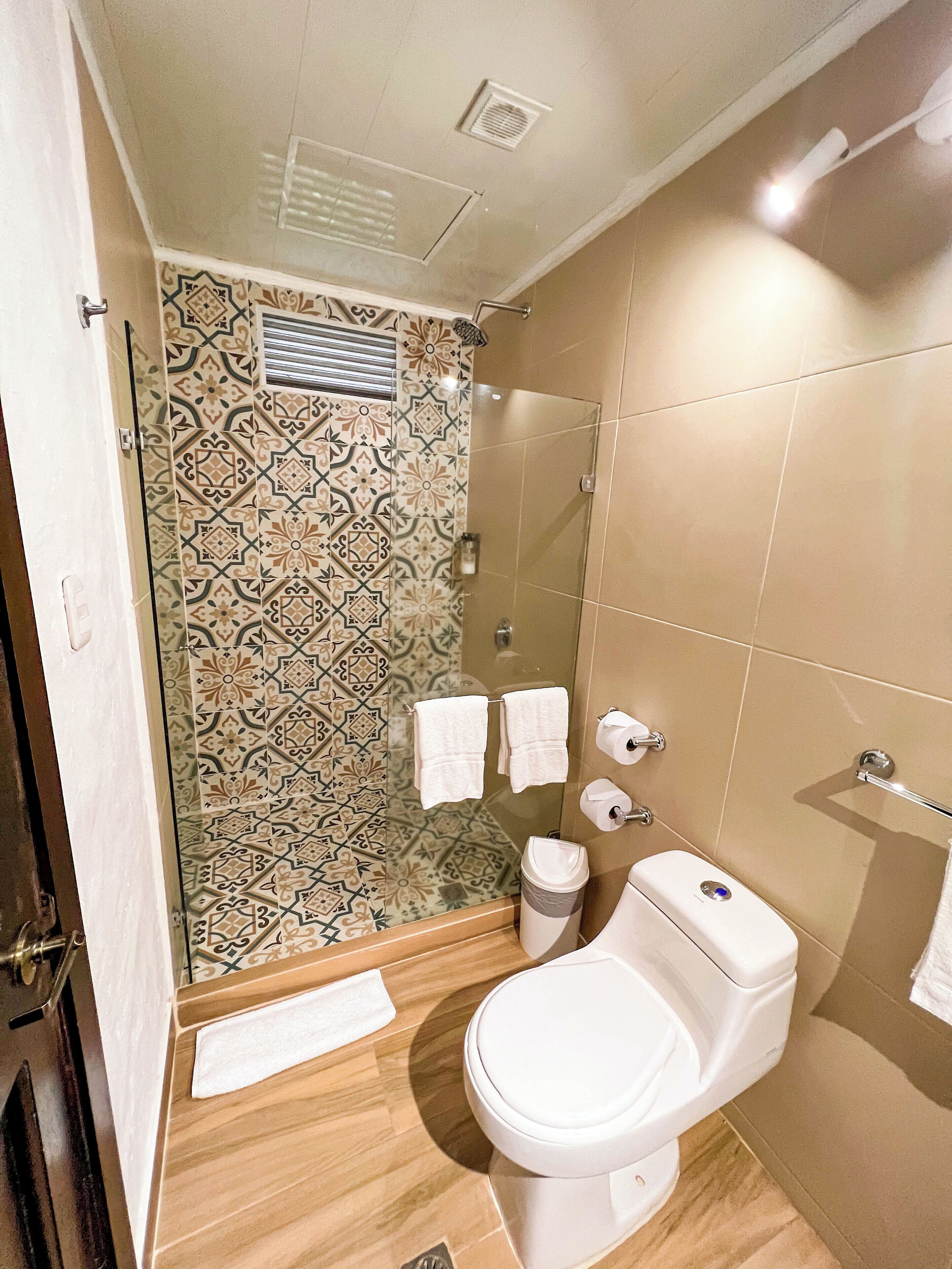 A bathroom with a patterned tile wall, a toilet, a glass shower enclosure, and a towel rack.