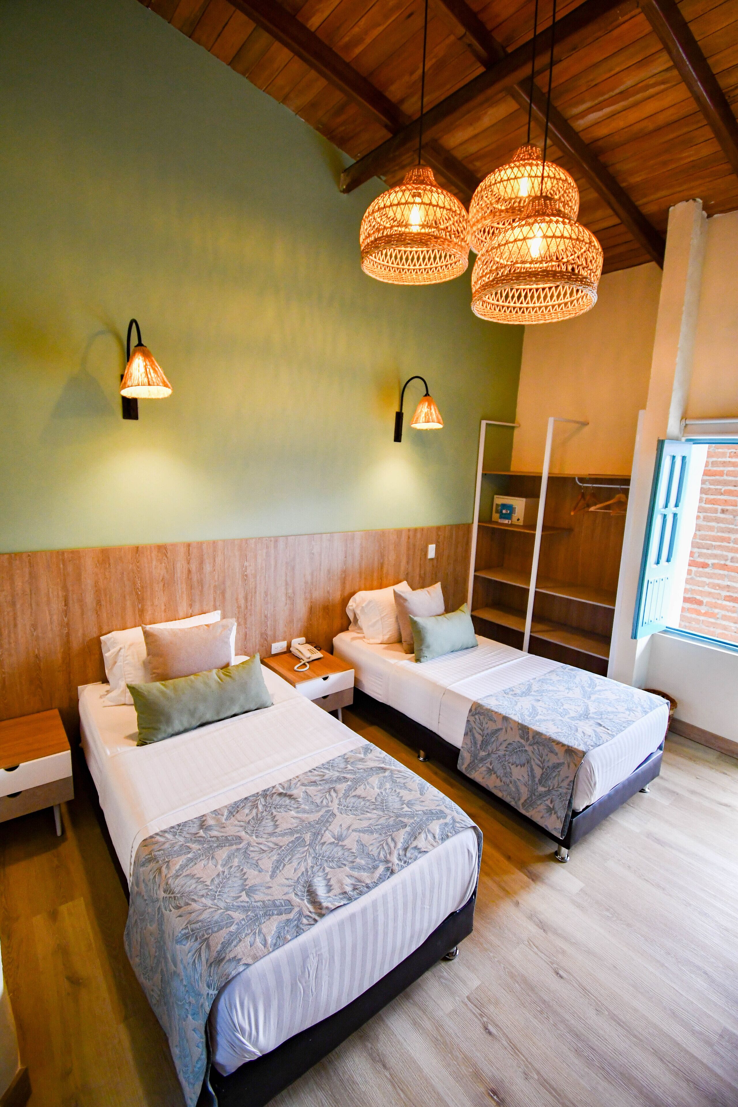 Habitación de hotel con dos camas, cabeceros de madera, techo de madera y lámparas colgantes de mimbre.