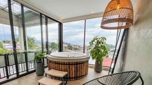 A modern balcony with a hot tub, wooden flooring, a wicker chair, and potted plants.