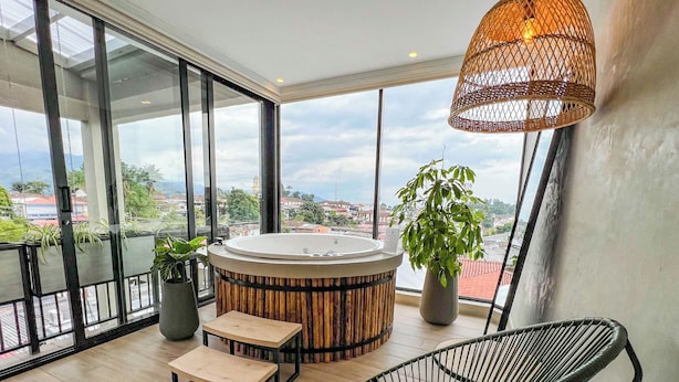 Un balcón moderno con jacuzzi, suelo de madera, una silla de mimbre y plantas en macetas.