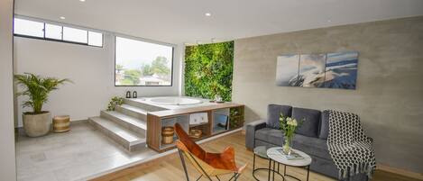 A modern living room with a sofa, a coffee table, a chair, a large window, a kitchen area with a sink, and a green wall.