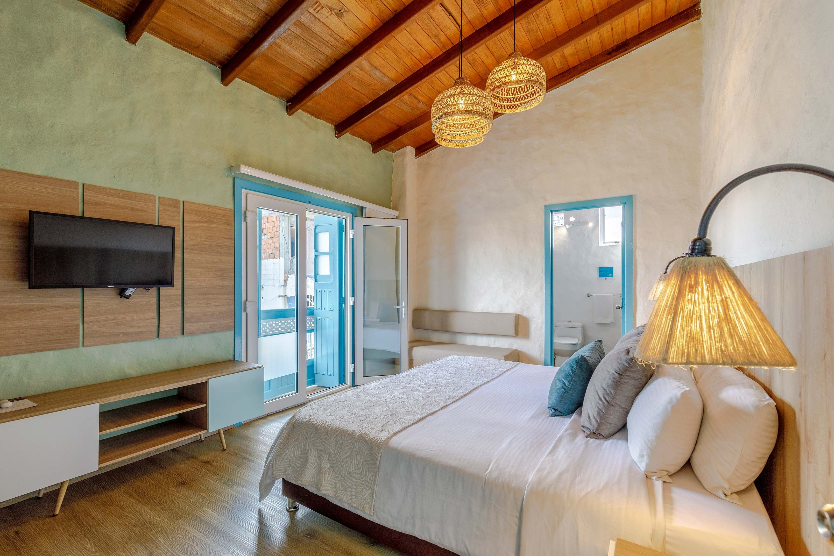 A bedroom with a bed, a TV, a desk, and a door leading to a balcony.