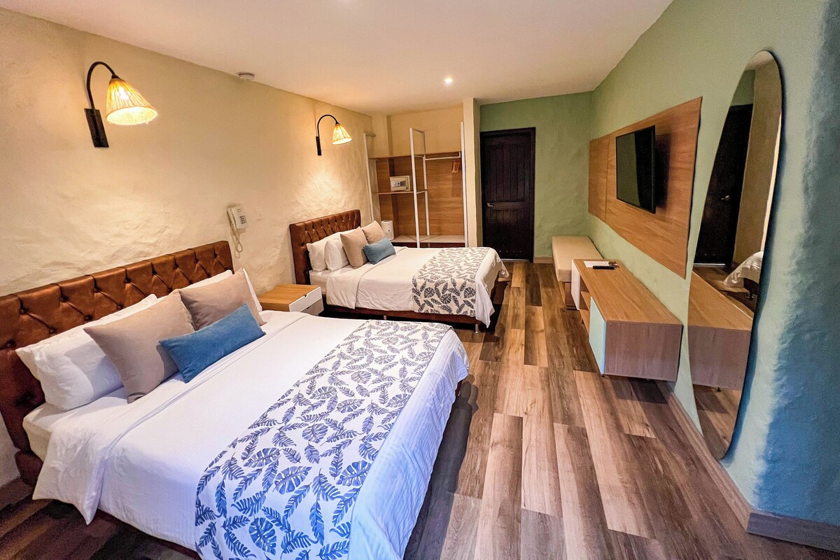 Habitación de hotel con dos camas, cabecera de madera, un banco, un espejo y un armario.