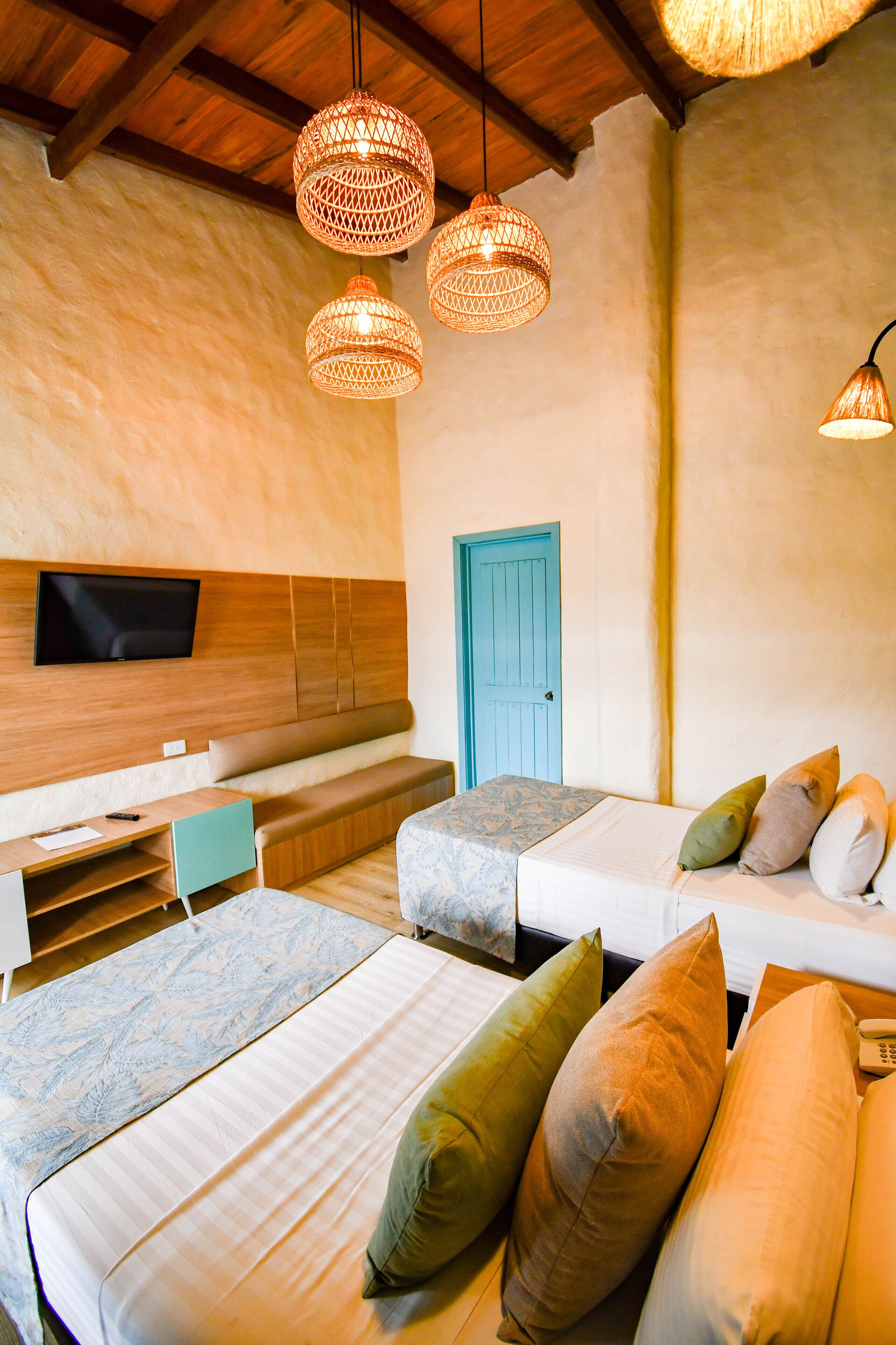 A room with two beds, a TV mounted on the wall, and a wooden ceiling.