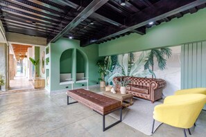 A spacious lobby with a high ceiling, a leather bench, a tufted sofa, and yellow armchairs.