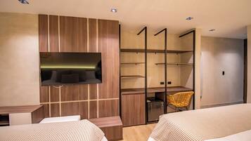 A modern hotel room with two beds, a TV mounted on a wooden panel, a small desk, and a chair.