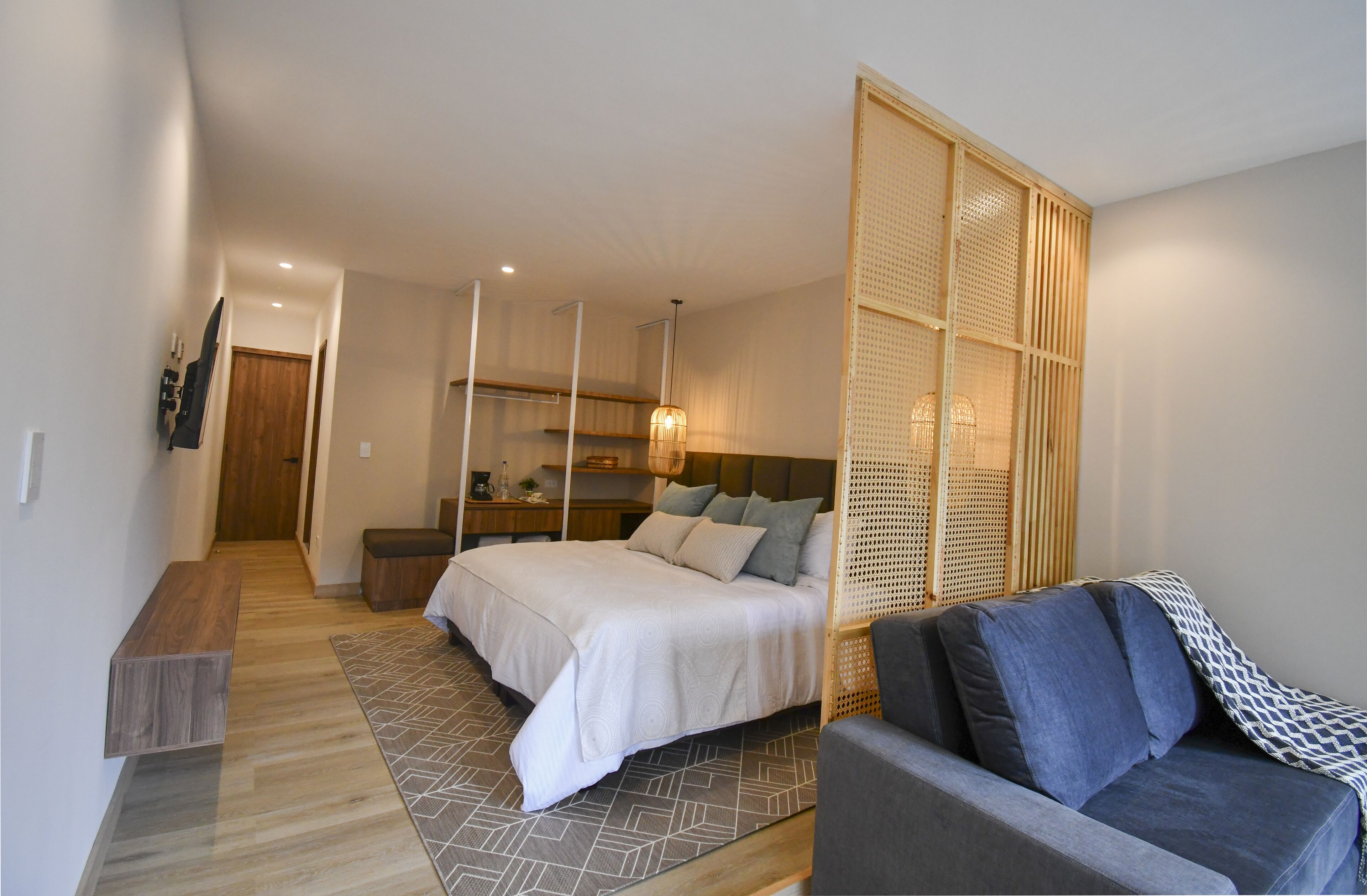 A modern bedroom with a large bed, a sofa, a wooden partition, and a desk with a lamp.