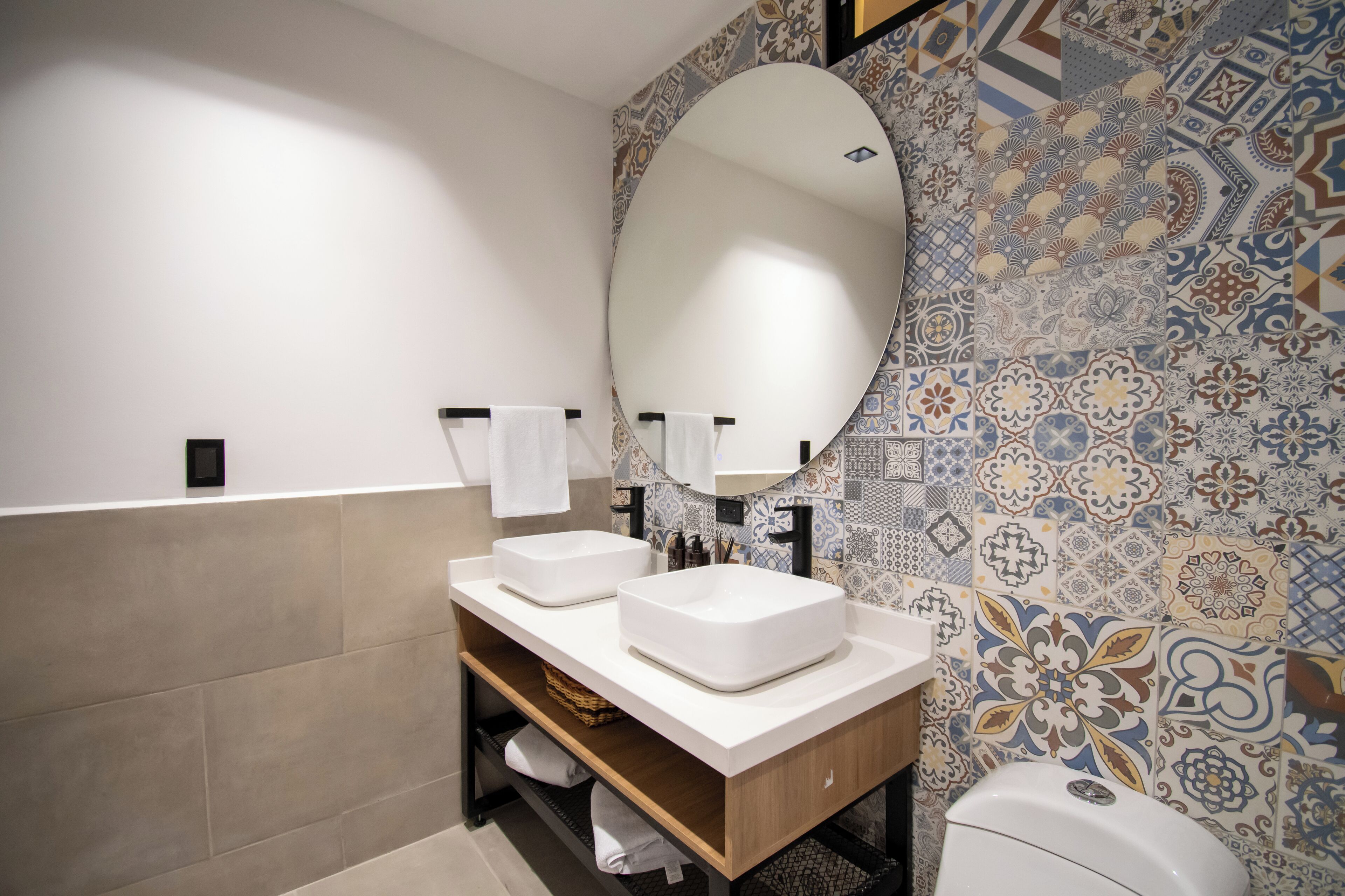 Une salle de bain moderne avec deux lavabos, un grand miroir et des murs recouverts de carreaux à motifs.