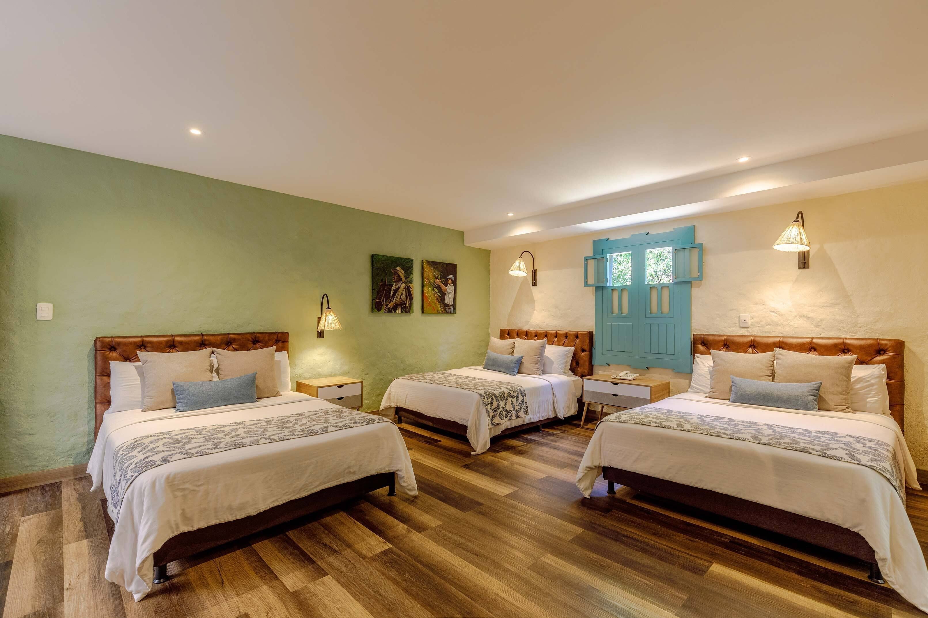 A hotel room with three beds, wooden flooring, and a blue door.