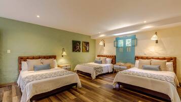 A hotel room with three beds, wooden flooring, and a blue door.