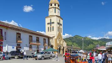Una iglesia con un campanario, una zona de mercado con gente y vehículos, y un pequeño coche naranja con una bandera.