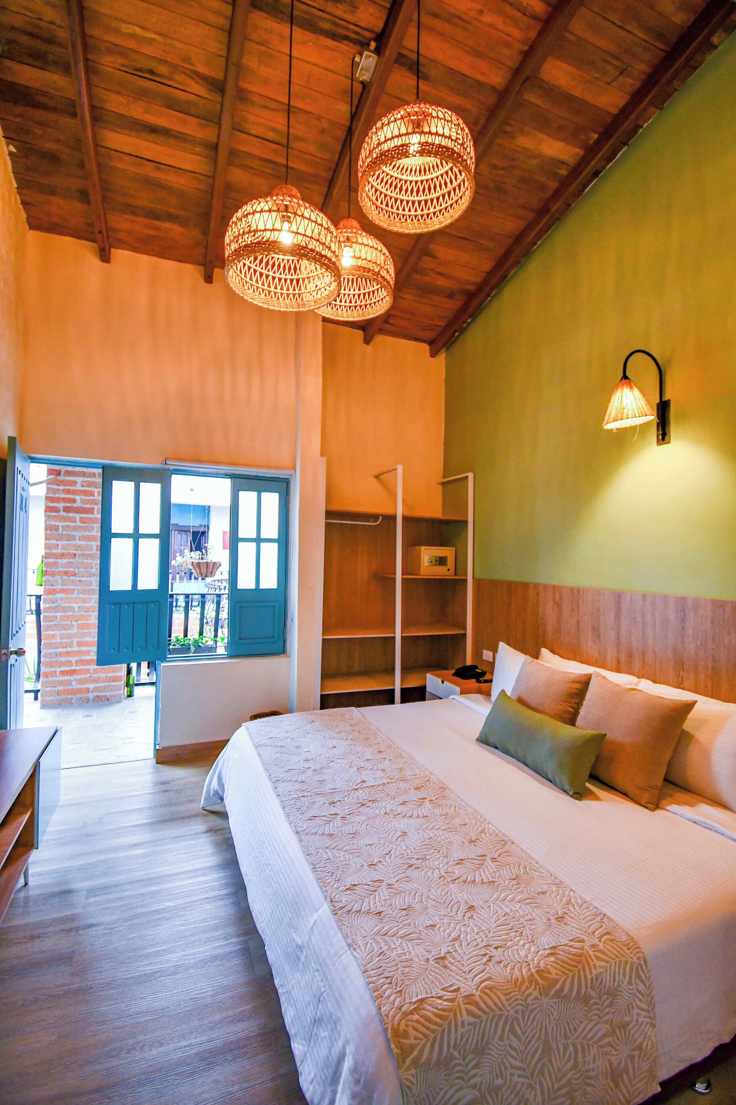 Quarto com cama grande, teto de madeira e vista através de uma porta.