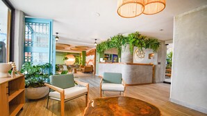 A spacious lobby with a reception desk, wooden chairs, a large wooden coffee table, and potted plants.