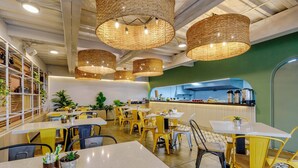 A restaurant interior with yellow chairs, white tables, and wicker pendant lights.