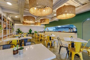 A restaurant interior with yellow chairs, white tables, and wicker pendant lights.