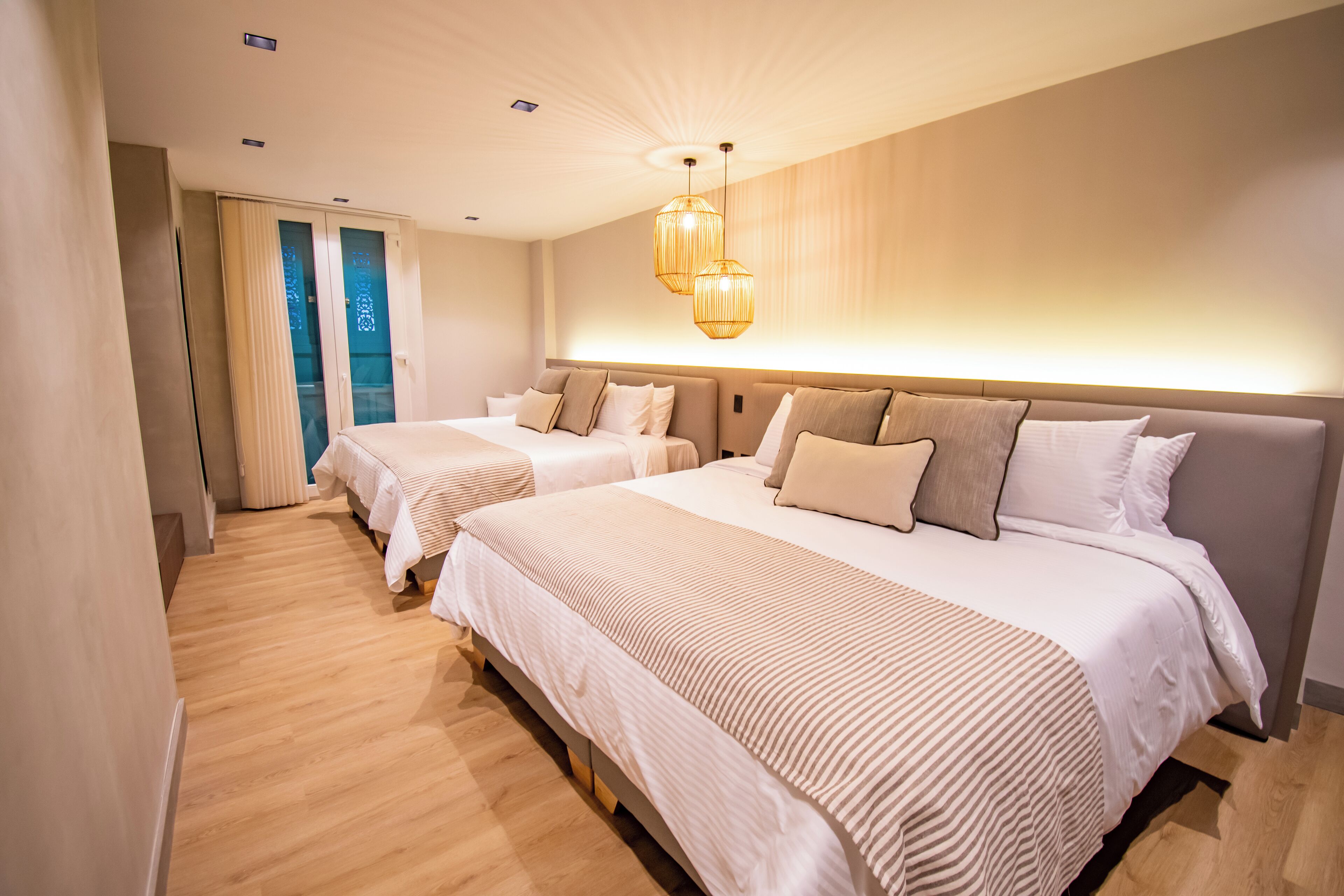A hotel room with two beds, a large window, and a modern chandelier.