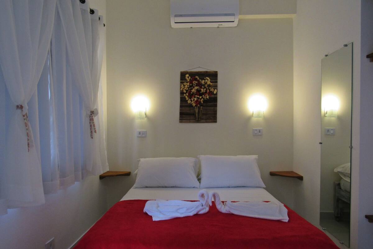 Une chambre d’hôtel comprenant un lit, deux tables de chevet, un climatiseur fixé au mur et un miroir.