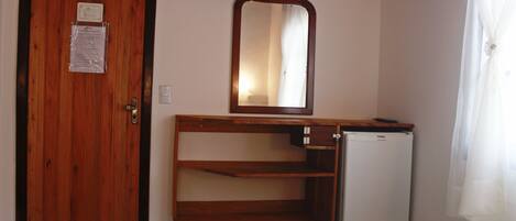A room with a wooden door, a small refrigerator, a mirror, and a bed with green bedding and towels.
