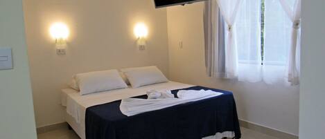 A hotel room with a bed, air conditioning unit, flat-screen TV, and a window with curtains.