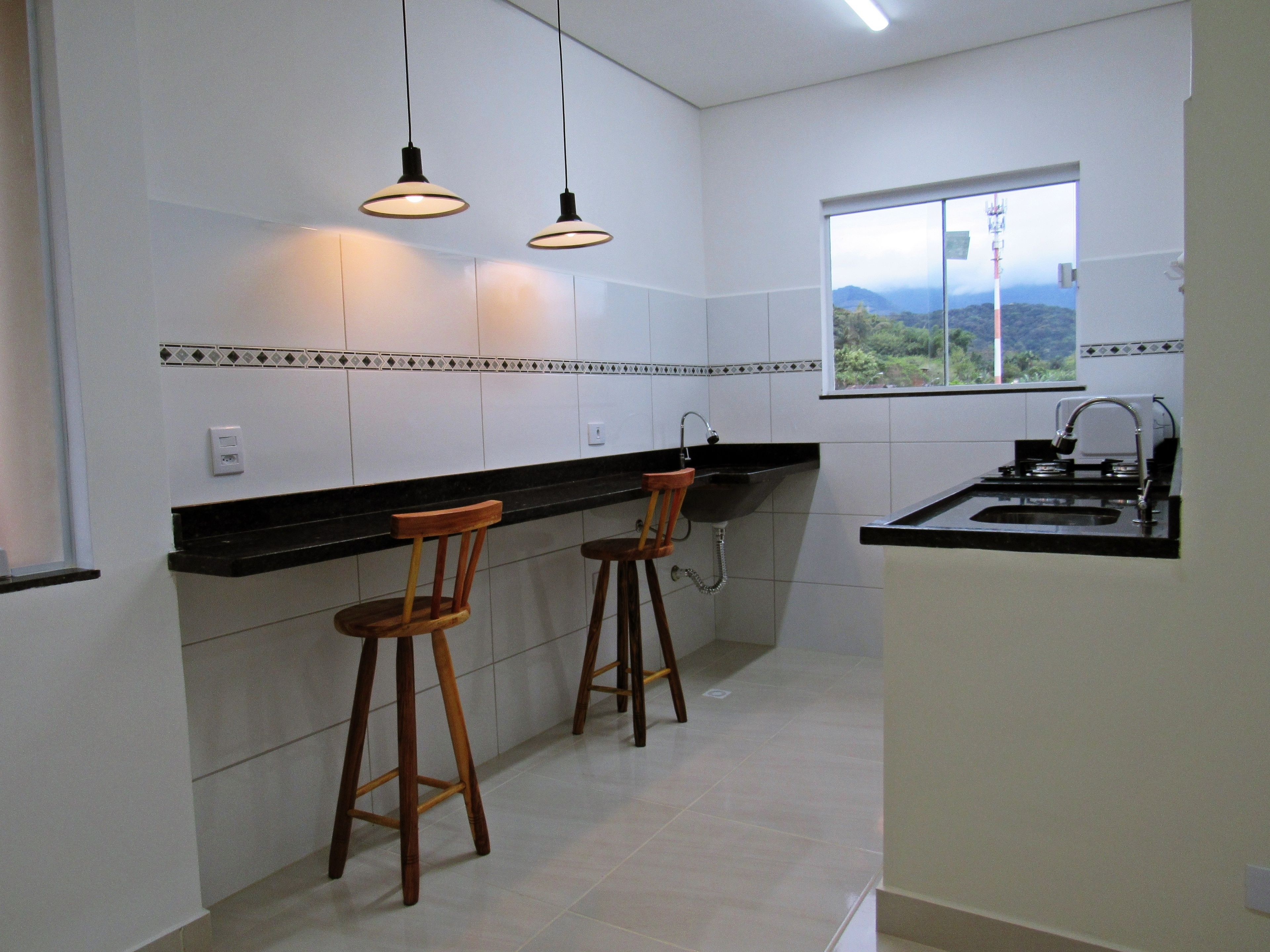 A kitchen with two wooden stools, a black countertop, and a window with a view of greenery.