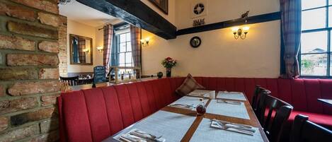 A restaurant with red upholstered booths, wooden tables with white placemats, and a brick wall.